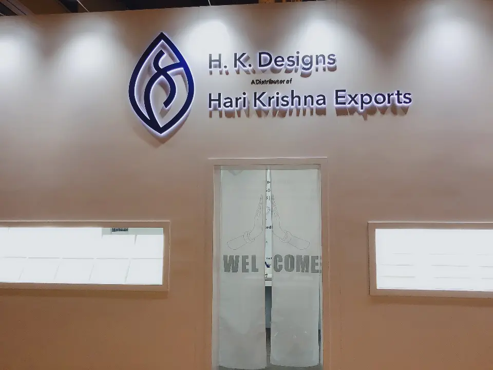 Close front view of the H.K. Designs and Hari Krishna Exports logo above a glass door