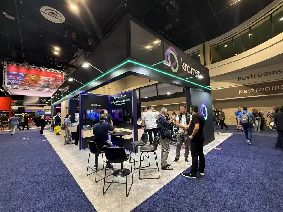 Kramer stand at InfoComm 2025 viewed down its length with glowing header trim and demo screens