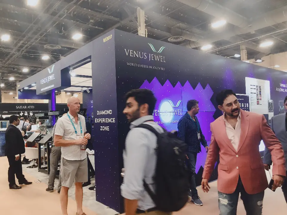 Visitors talking in front of a purple glowing wall at the Venus Jewel booth