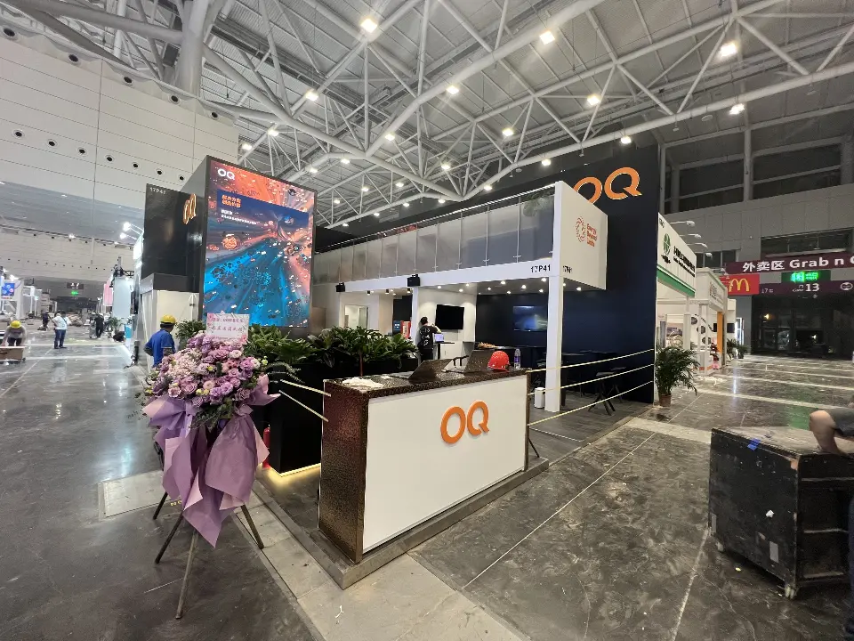 Front of the booth with OQ counter, plants and the tall video screen behind