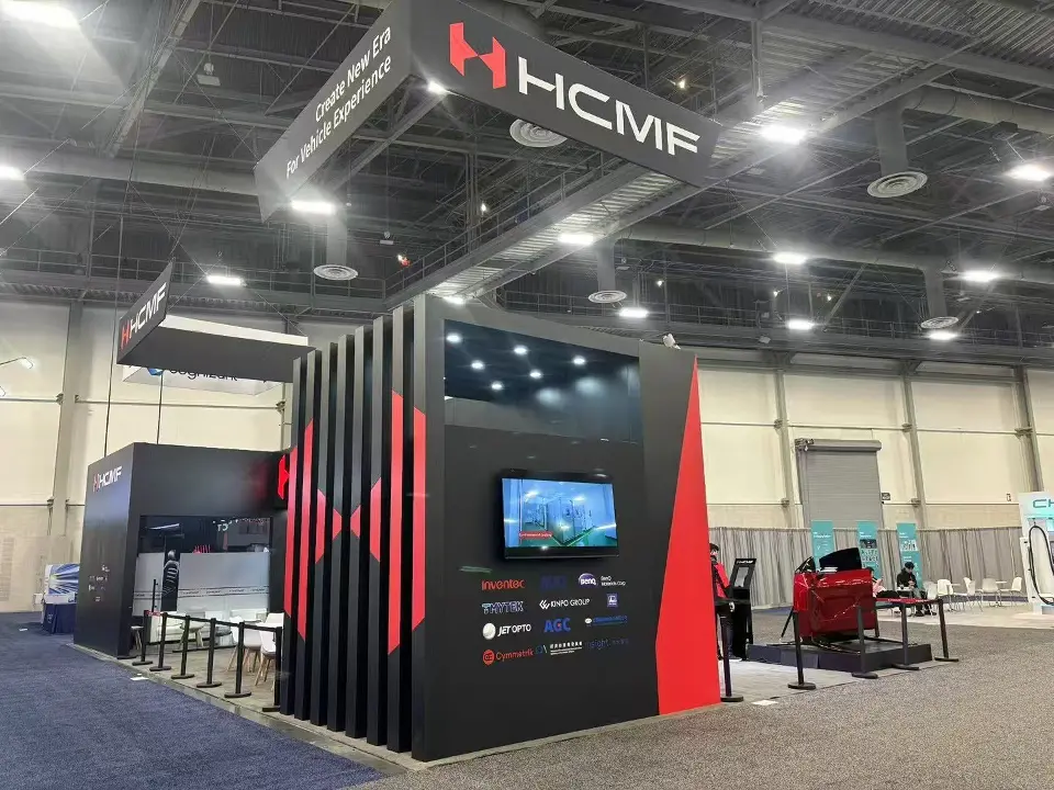 Corner of black slatted walls with the HCMF header and a wall-mounted screen