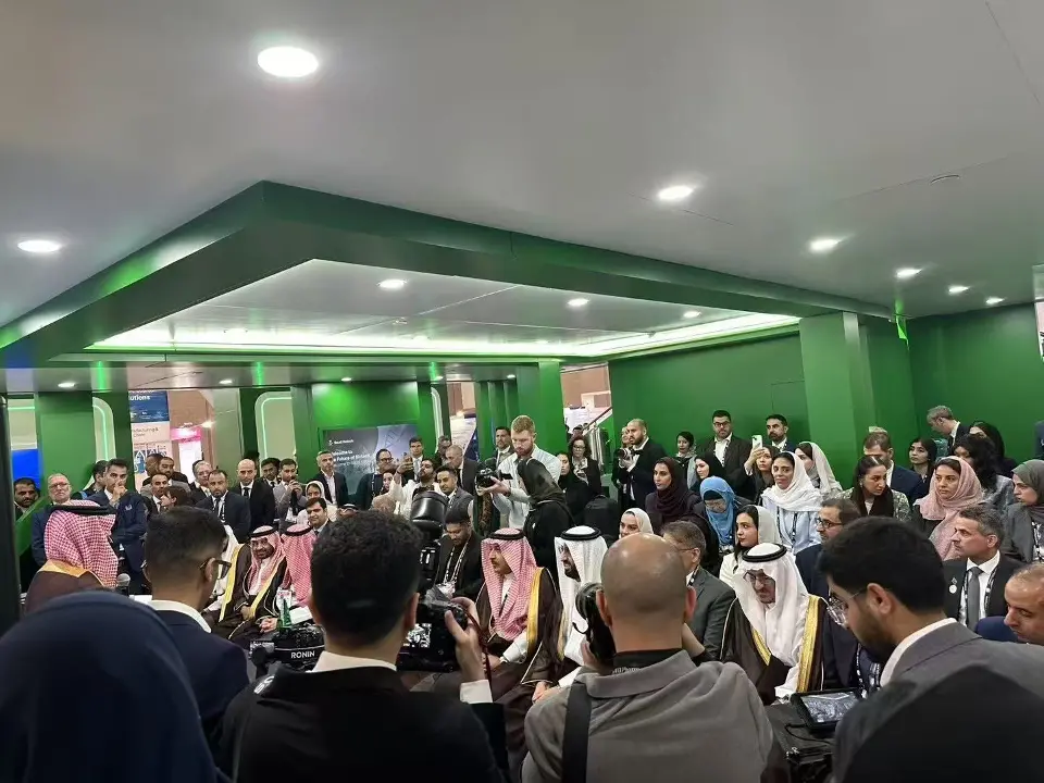 Packed session inside the green meeting area with a lit ceiling edge