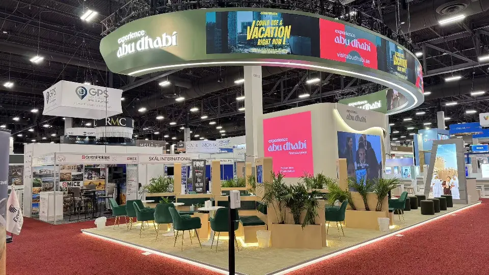 Abu Dhabi booth with curved ring of video screens over green chairs and palm planters
