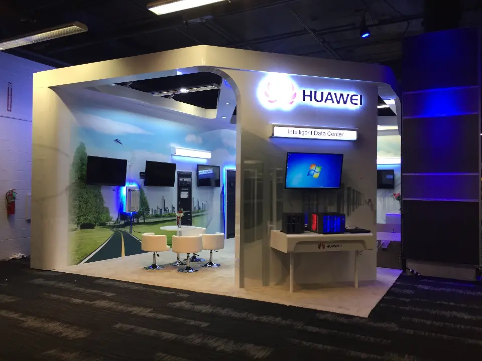 Huawei booth front with a lit logo, wall screen and white display table