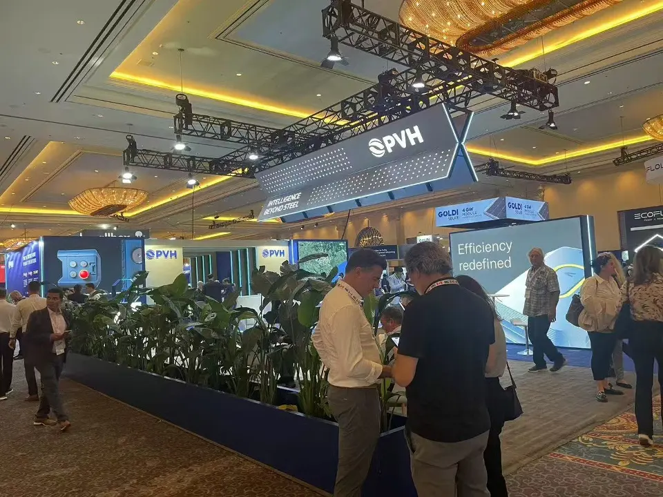 PVH booth with blue walls, angled hanging sign, planters and visitors talking in front