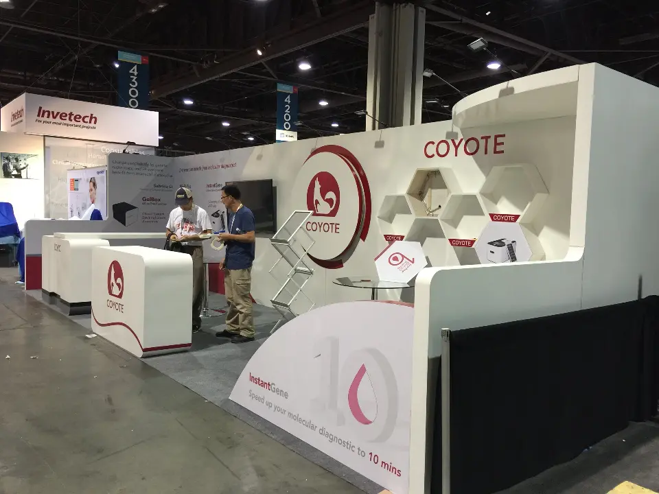 Wide view of COYOTE white booth with curved counters, hexagon shelves and screen