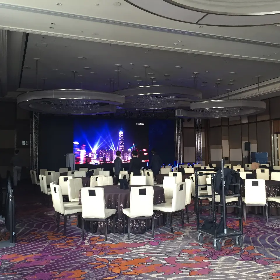 Ballroom set with round tables in white chair covers facing the lit stage