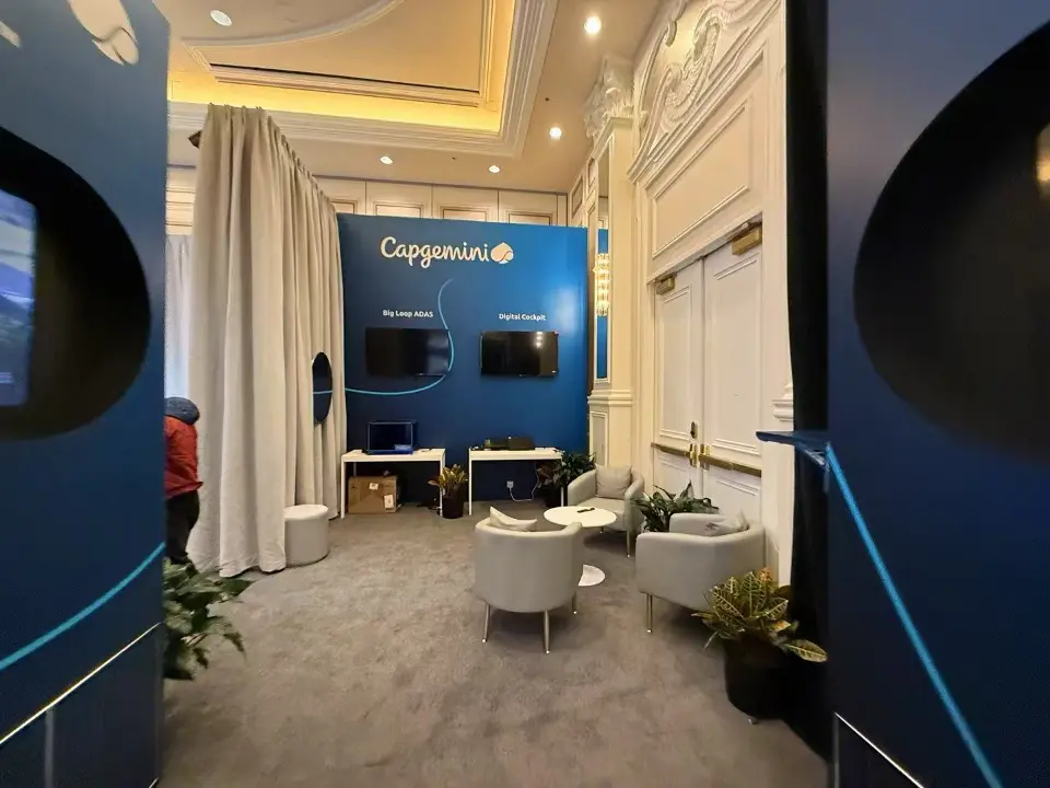 Curtained lounge area with white armchairs and a Capgemini wall screen