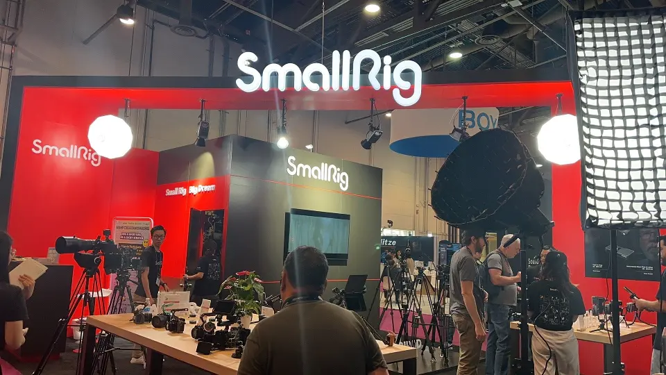 Red back wall with white SmallRig logo above tables of camera accessories and softboxes