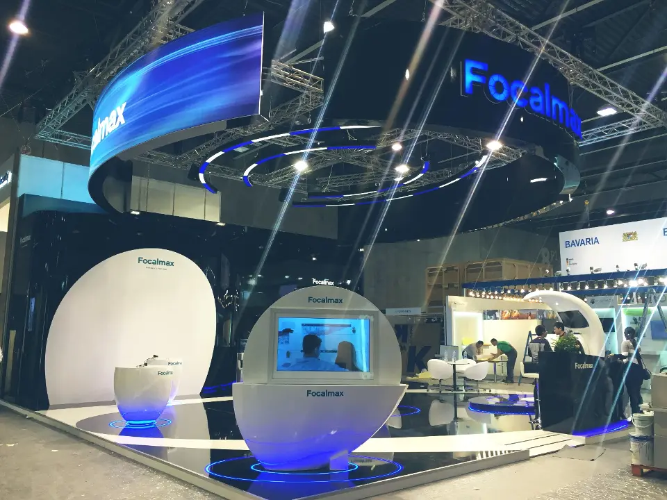 Focalmax stand at MWC 2016 under a black hanging ring with a curved blue banner and white egg-shaped kiosks