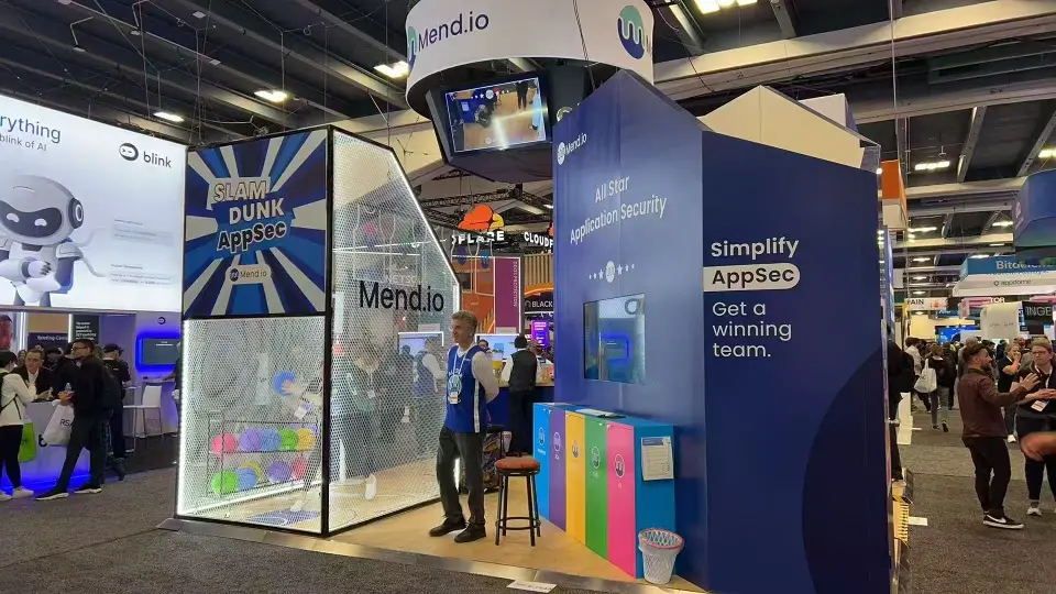 Mend.io glass game booth beside a navy Simplify AppSec wall and coloured lockers