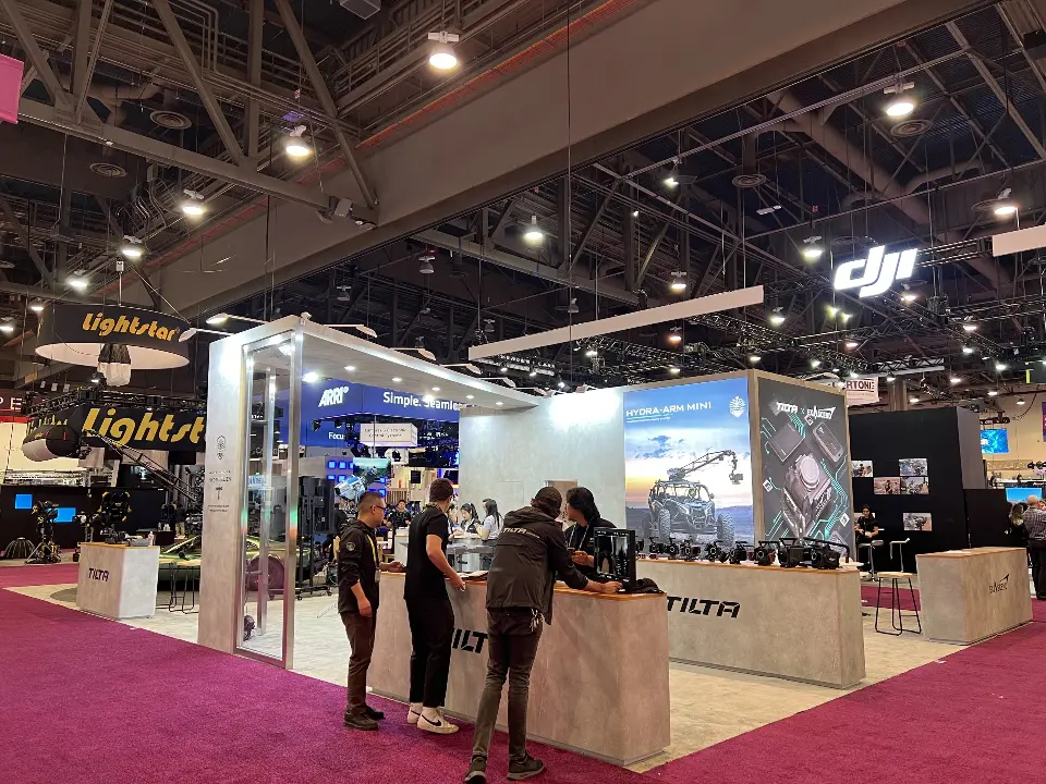 Visitors at a Tilta demo counter with rigged cameras and backlit Hydra-Arm Mini graphic