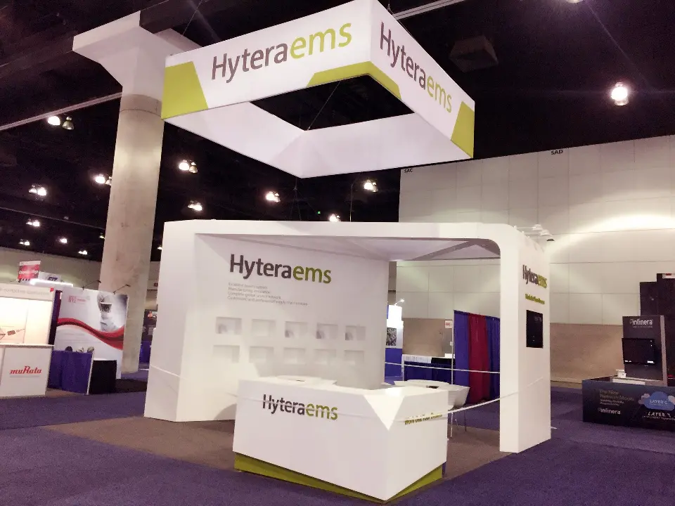 Hyteraems booth front with curved white walls, logo counter and square hanging sign above