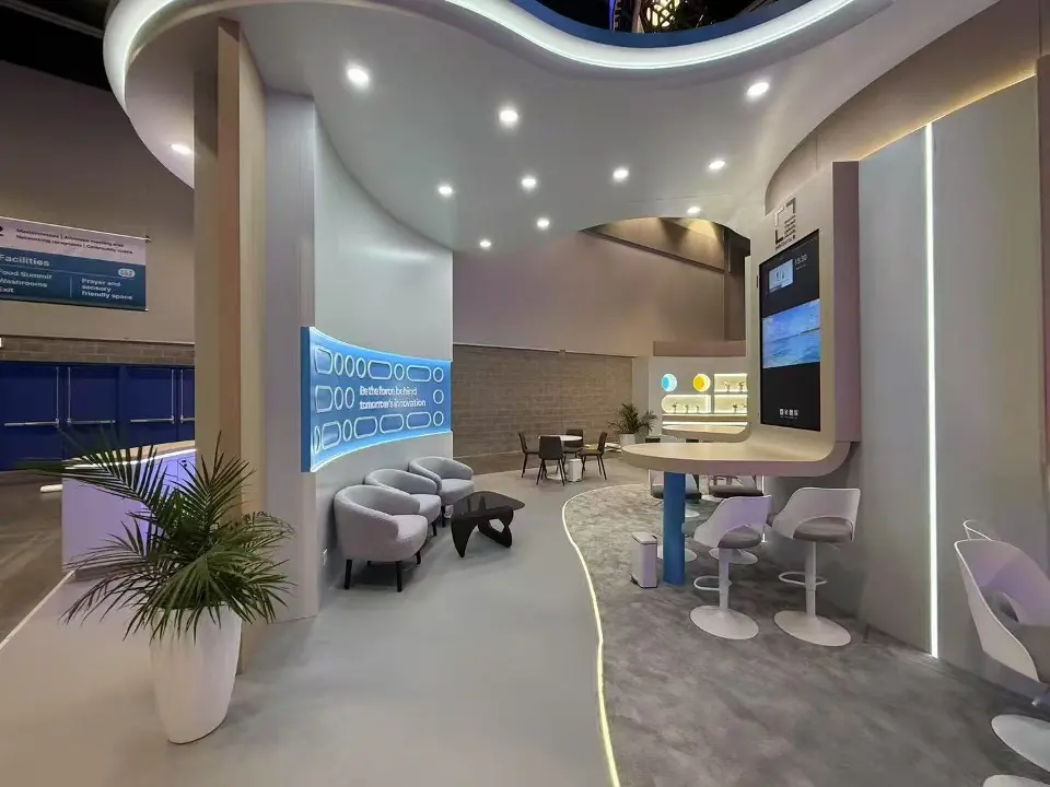Lounge area with grey sofas, a plant and a curved backlit wall inside the booth