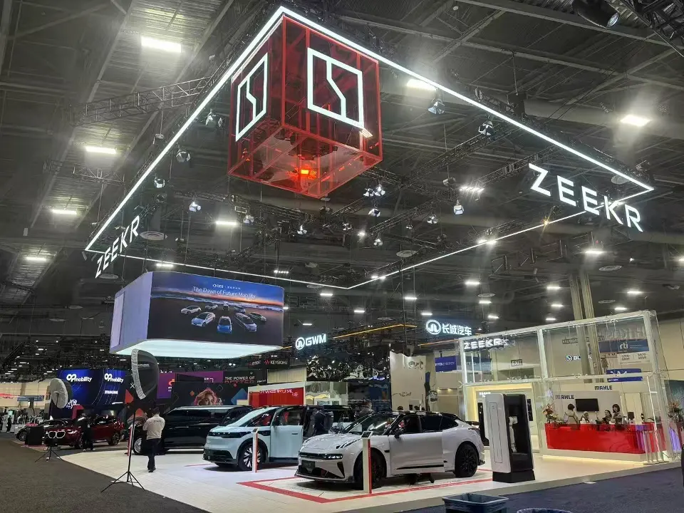 Wide view of the ZEEKR stand with a red logo cube, parked vehicles and glass display boxes