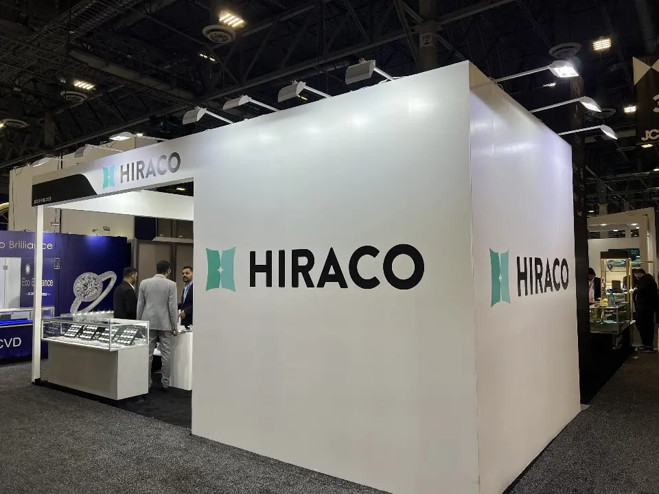 Closed white block of the HIRACO booth with large teal logos and arm lights along the top