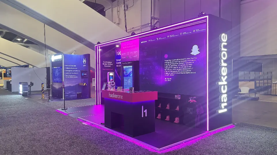 Angled view of the HackerOne stand with pink counter and kiosk screen