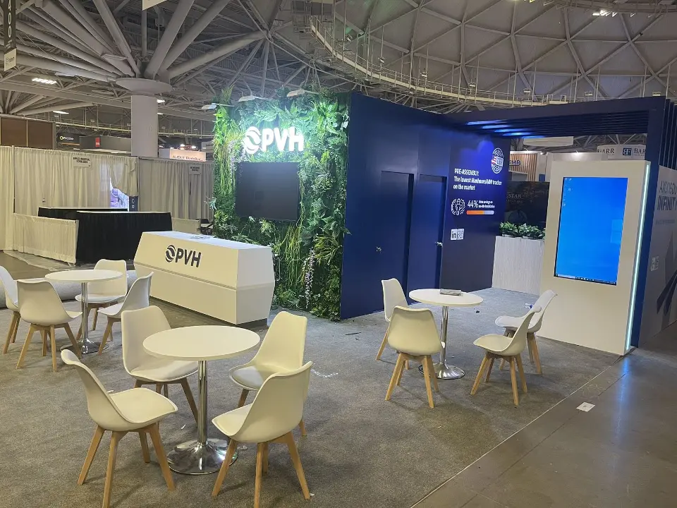 Navy booth with green plant wall and PVH logo, white counter, tables and chairs
