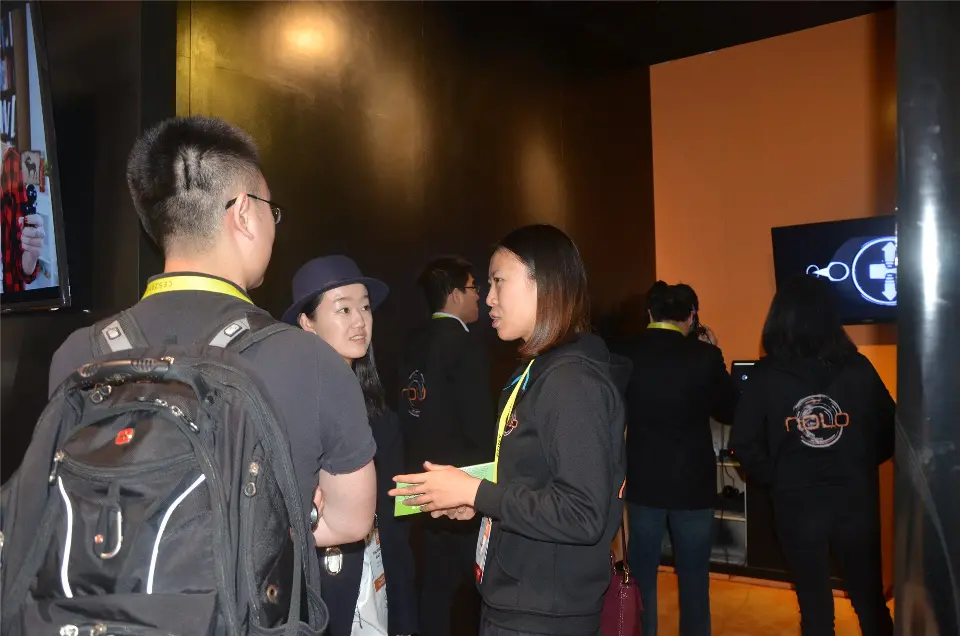 Visitors talking inside the booth beside an orange-lit wall and screen