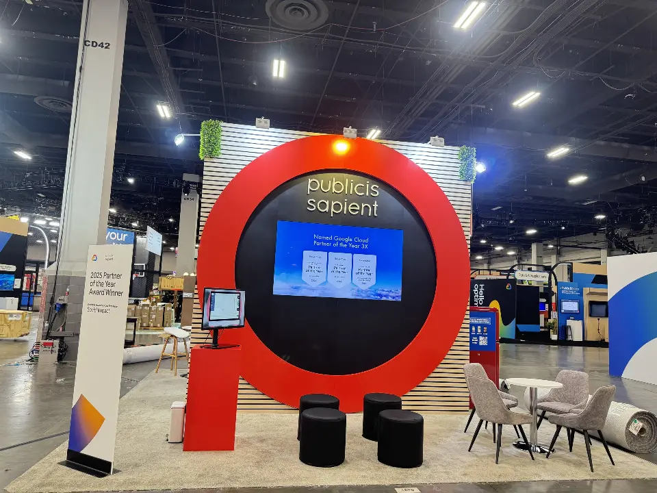 Front view of Publicis Sapient booth with red ring frame, video screen and black stools