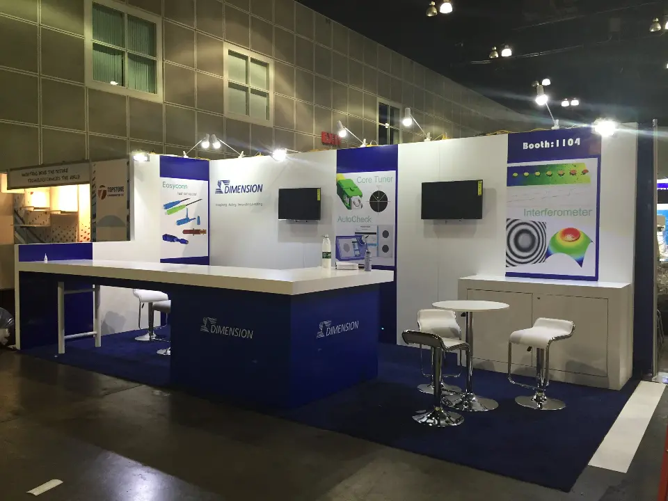 Wide view of the Dimension booth showing bar seating, screens and round graphic