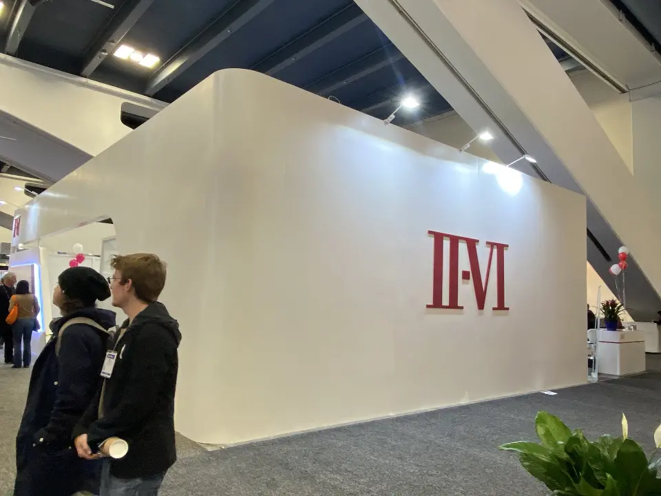 Rounded white wall with red II-VI lettering and visitors looking on