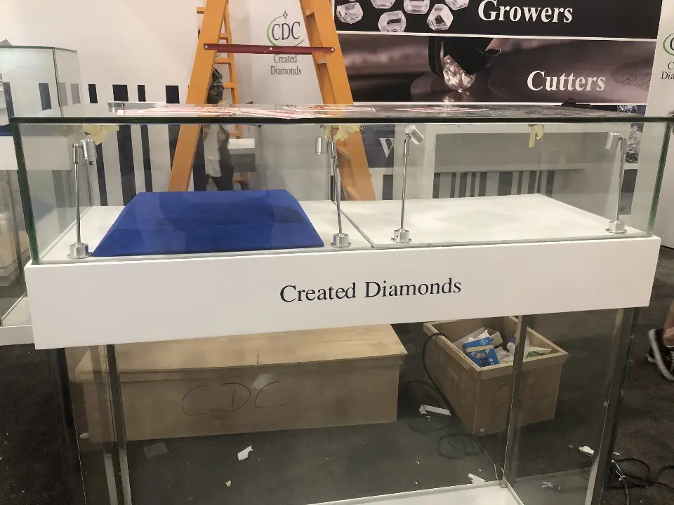 Glass jewelry showcase with blue velvet trays on a white Created Diamonds base