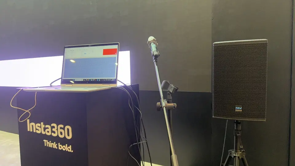 Black presenter podium with laptop, microphone and speaker against a lit wall
