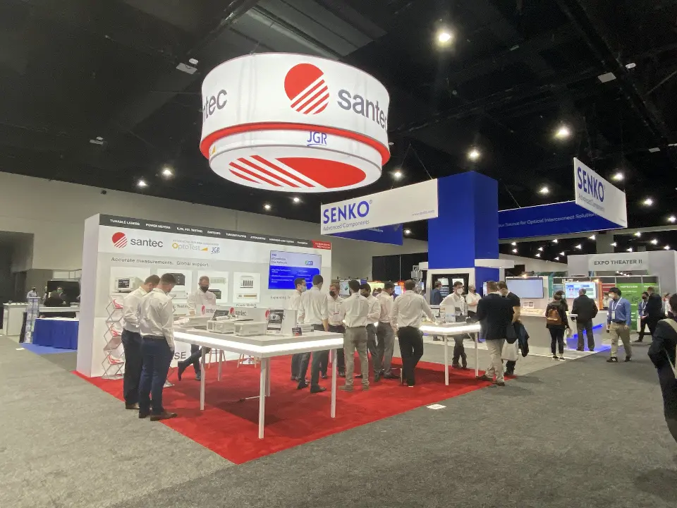 Visitors at white product tables on red carpet under the round santec sign