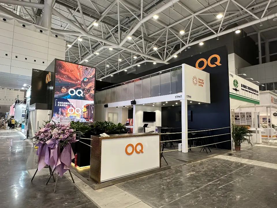 Wider view of the OQ booth with video screen, glass balustrade and plants