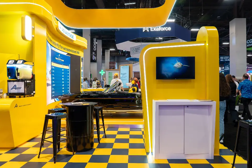 Yellow side wall of the Advantage booth with a slush machine, a screen pillar and high tables