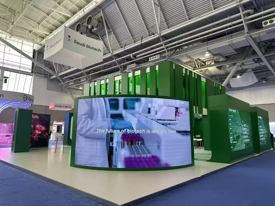 Curved green-framed screen showing lab imagery with the pavilion walls behind