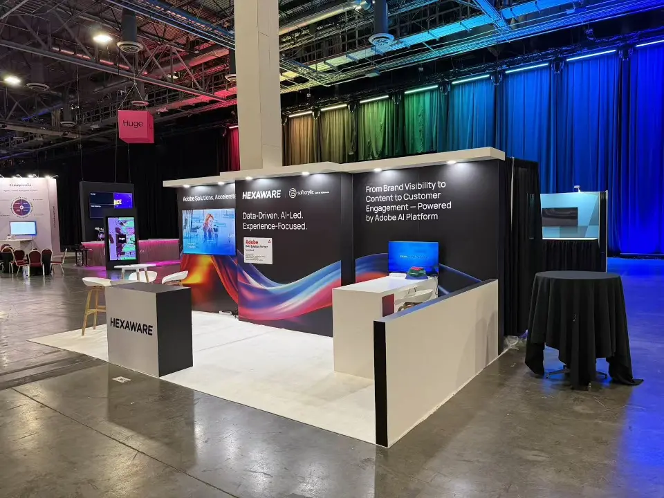 Hexaware booth from the open side with white counter, black graphic walls and two screens