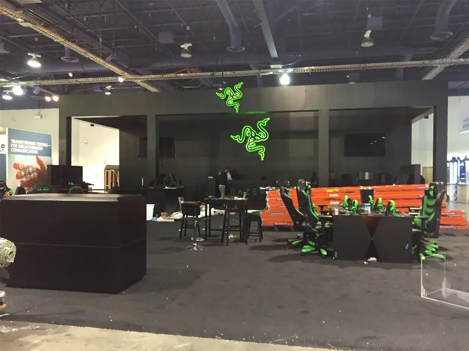 During build-up: black frame with lit green logos, gaming chairs and stacked ladders