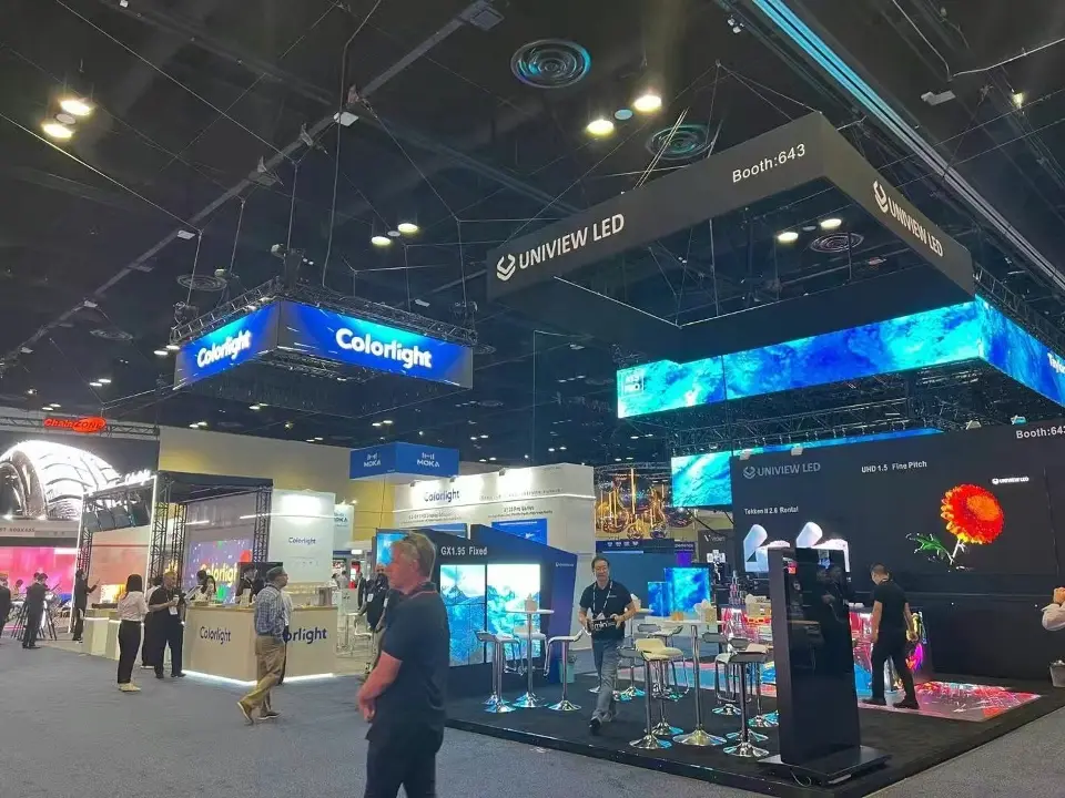 Hall view of the Colorlight booth with suspended screen headers, black walls and visitors