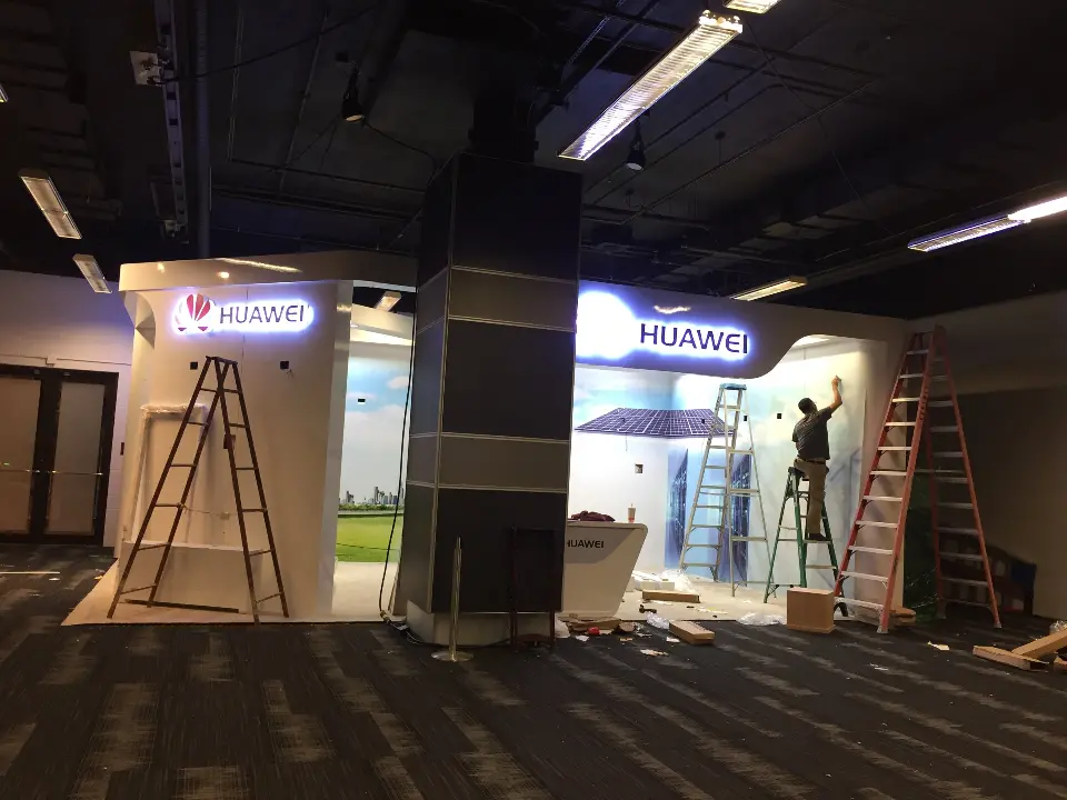 During installation: Huawei booth walls with a lit logo while crew work from two ladders