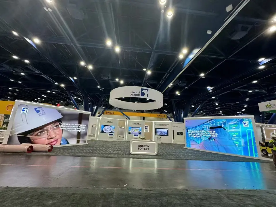 ADNOC booth front with two large backlit graphics and the ring sign overhead