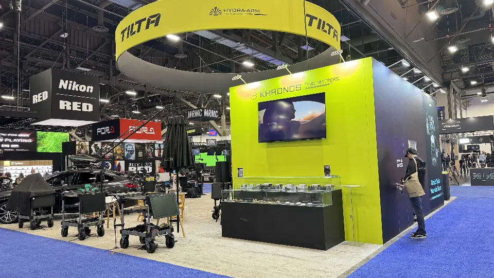 Yellow-green cube wall of the Tilta booth with a mounted screen and glass product cases
