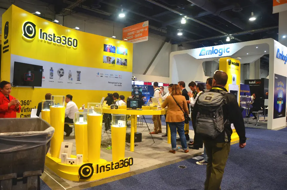 Yellow acrylic-topped camera plinths in front of the backlit Insta360 logo wall, with visitors