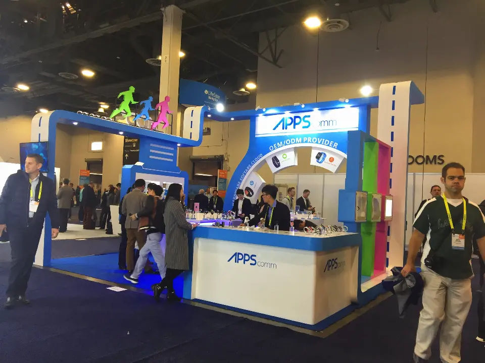 Front of the APPScomm booth with running-figure sculptures on top and visitors