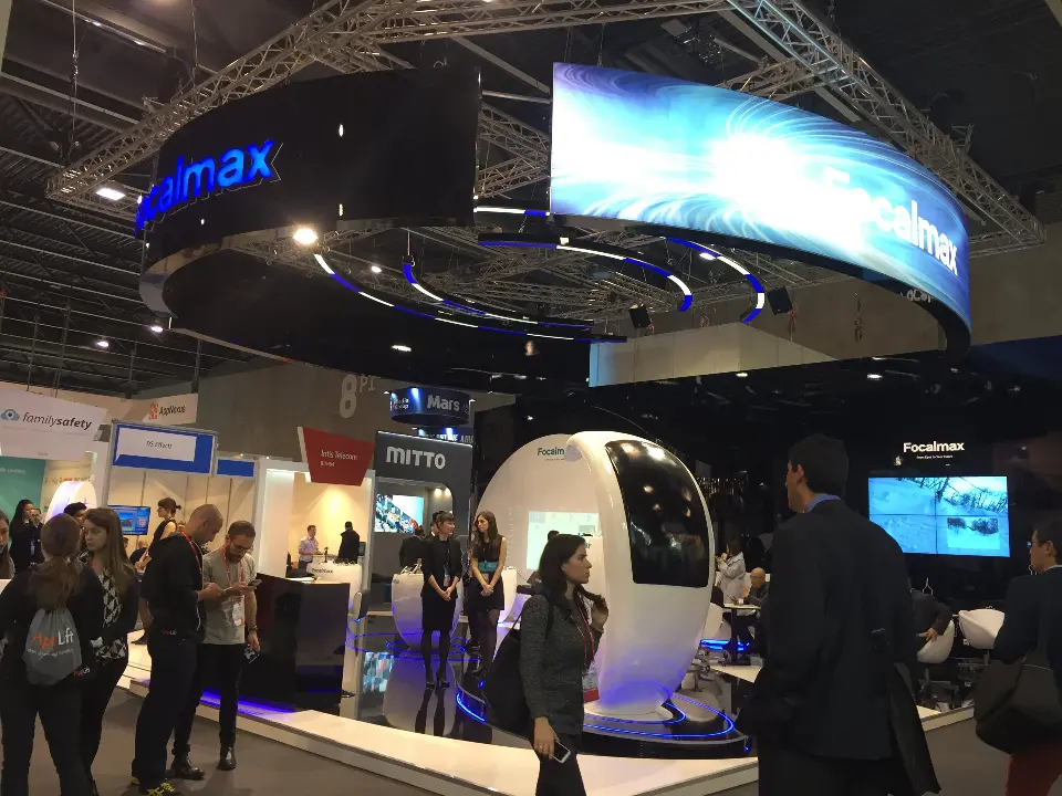 Side view of the stand with white pod chairs and a screen kiosk among visitors
