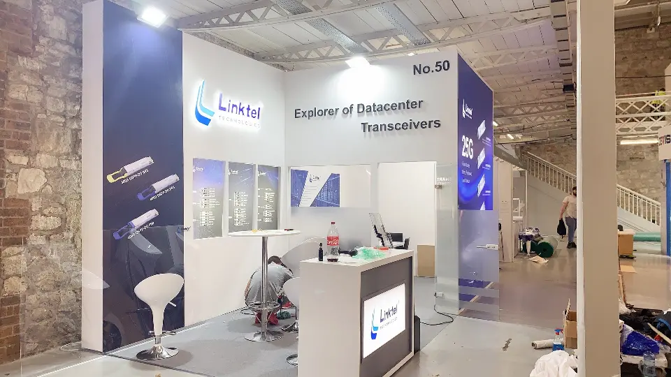 During build-up: white Linktel corner booth with counter, stool and tagline wall