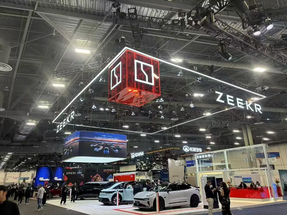 Wide view of the ZEEKR booth with lit outline frame, red cube sign and vehicles