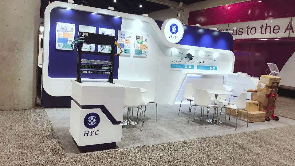 Curved white booth with lit round HYC logo, rack display plinth and white chairs