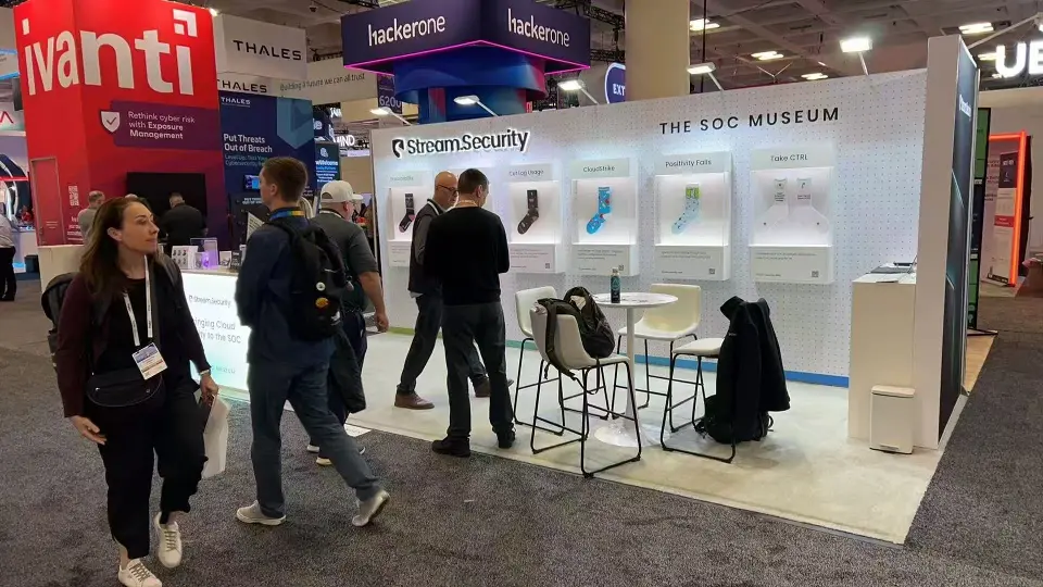 Stream.Security stand at RSAC from the aisle with visitors passing the white SOC Museum wall