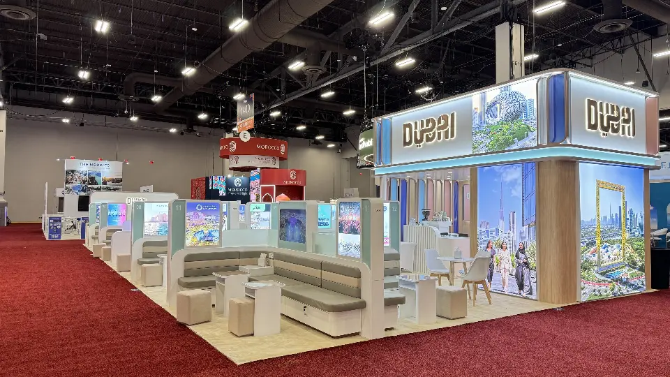Dubai Pavilion tower with Dubai lettering and city graphics above rows of grey meeting booths