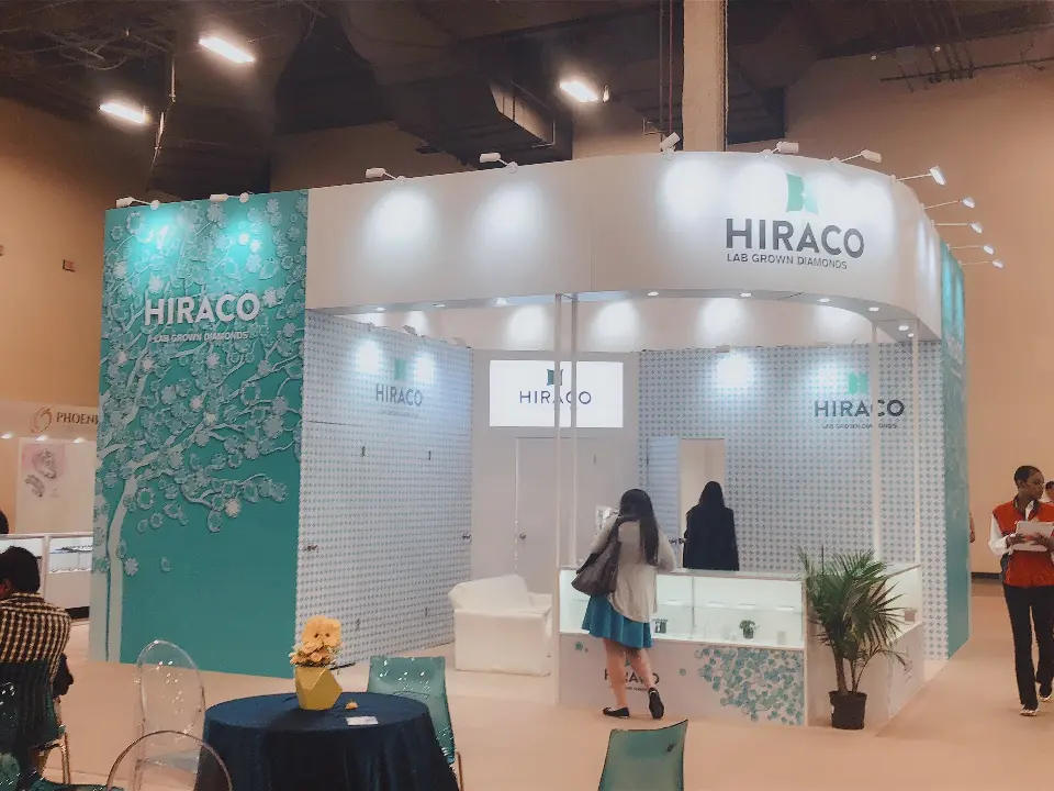 Show-day view of visitors at HIRACO glass showcases beside the teal patterned corner