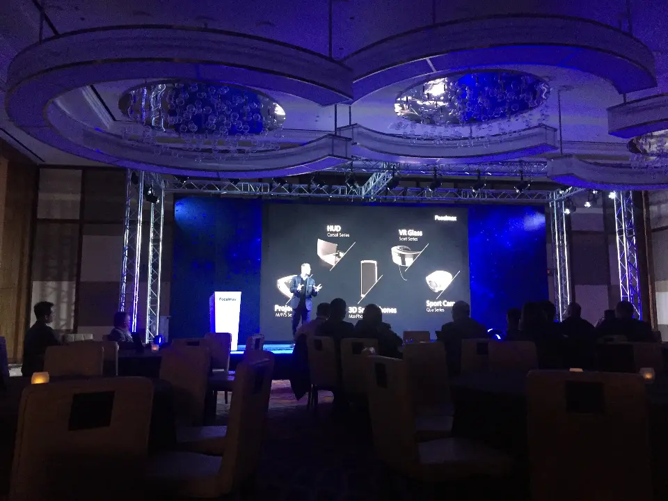 Presenter on the lit stage in front of a product graphic on the video screen