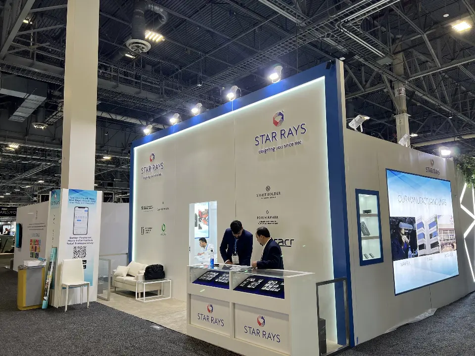 Star Rays booth with blue-framed white wall, partner logos, showcase counter and backlit manufacturing graphic