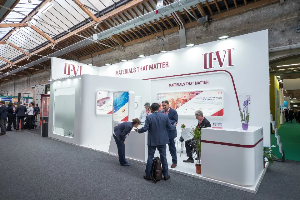 Visitors in conversation along the open front of the curved white booth